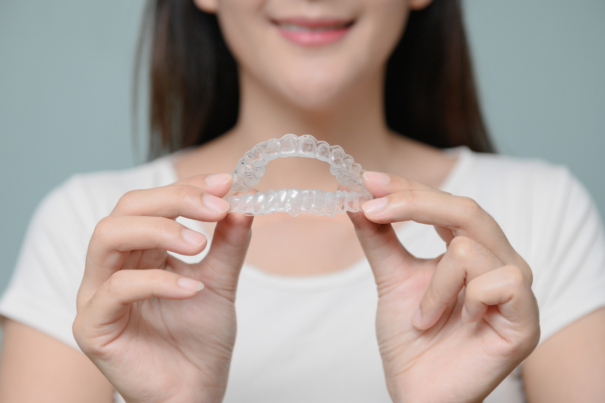 Woman holding a custom clear night guard for teeth grinding, comparing custom vs. boil-and-bite night guards