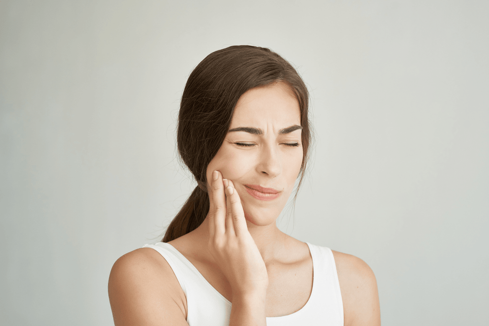 Woman touching her jaw in pain while experiencing possible TMJ disorder symptoms
