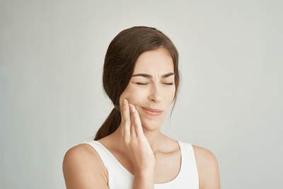 Woman touching her jaw in pain while experiencing possible TMJ disorder symptoms