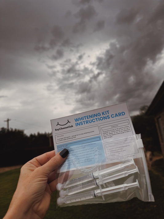 SayCheeseClub Teeth Whitening Kit Held in Air — clouds in background