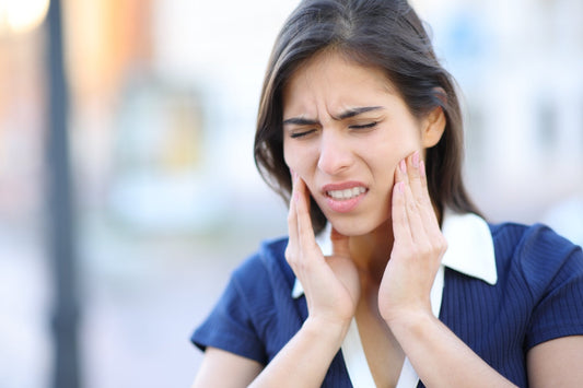 woman pressing both hands to her jaw with a pained expression, suggesting tooth or jaw discomfort.