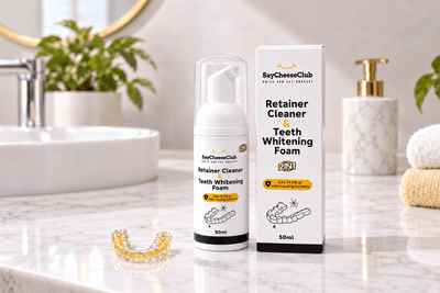SayCheeseClub Retainer Cleaner and Teeth Whitening Foam with a yellow-stained clear retainer on a bathroom counter.