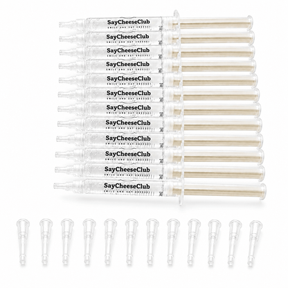 A set of twelve clear plastic syringe-style containers labeled SayCheeseClub, arranged in a row above ten matching clear applicator tips on a white background.