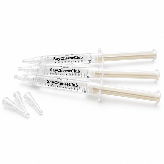 Three clear plastic syringes labeled SayCheeseClub Whitening Gel, with three small clear applicator tips placed beside them on a white background.