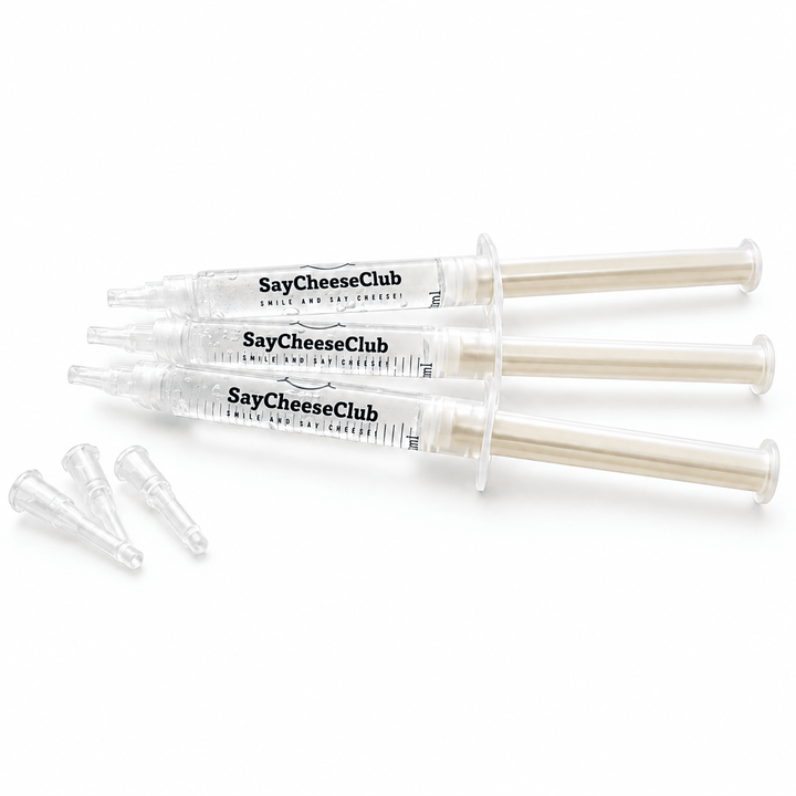 Three clear plastic syringes labeled SayCheeseClub Whitening Gel, with three small clear applicator tips placed beside them on a white background.