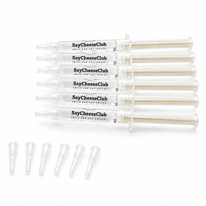 Five clear plastic syringe-style tubes labeled SayCheeseClub, arranged horizontally on a white background, with five small clear applicator tips lined up below.
