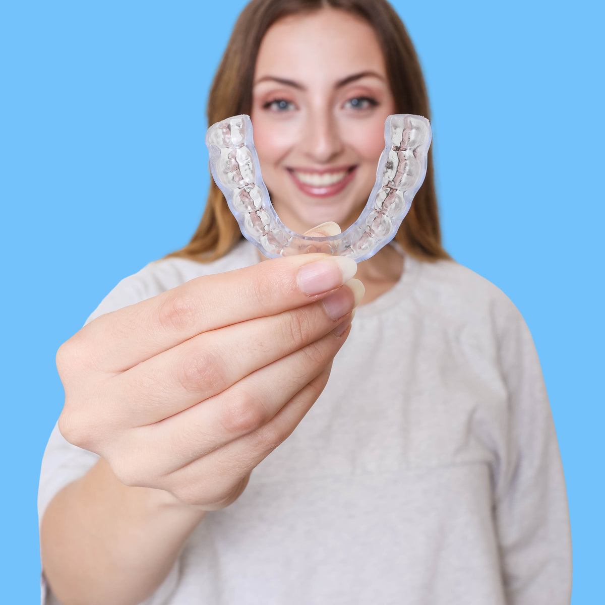 Woman holding a clear dental aligner against a blue background