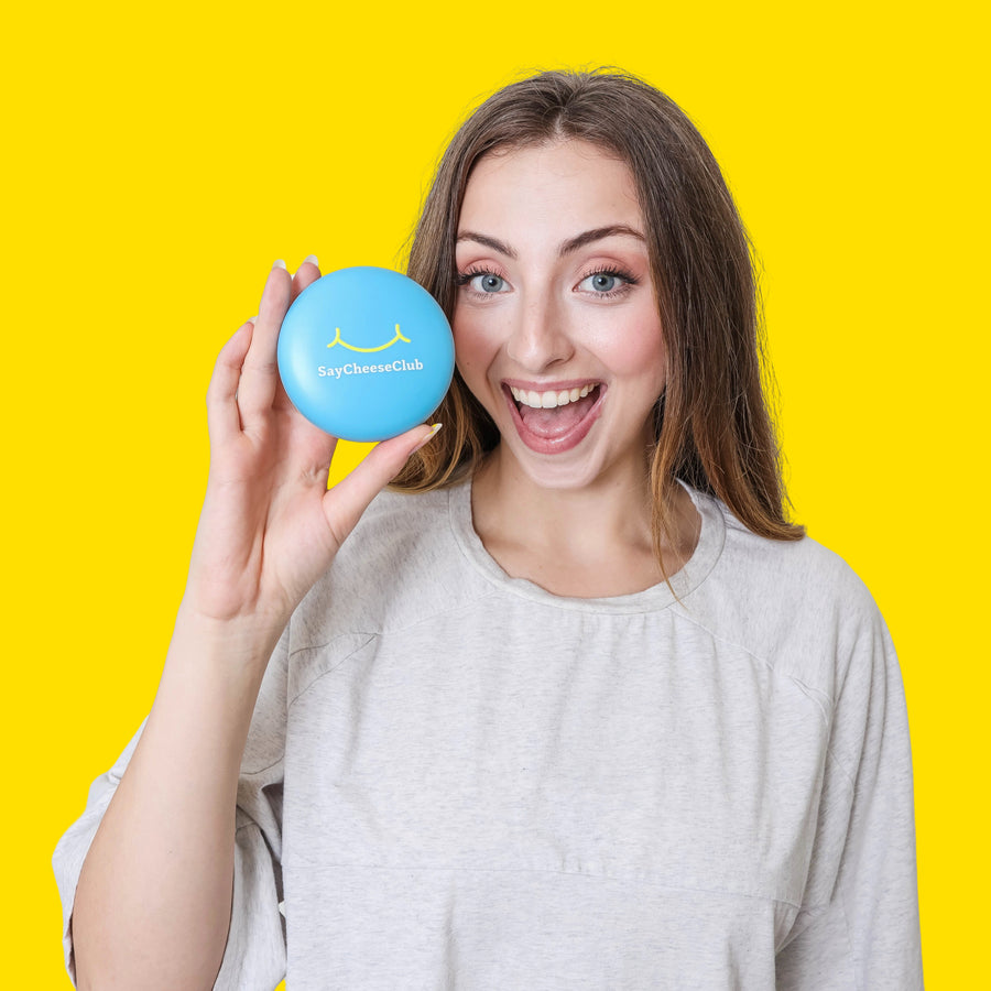 Woman holding a blue retainer case with a smiley face on a yellow background