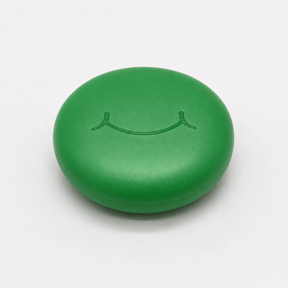A round green hard retainer case with a simple embossed smiley face on top, photographed on a clean white background.  Also good for clear aligner case.