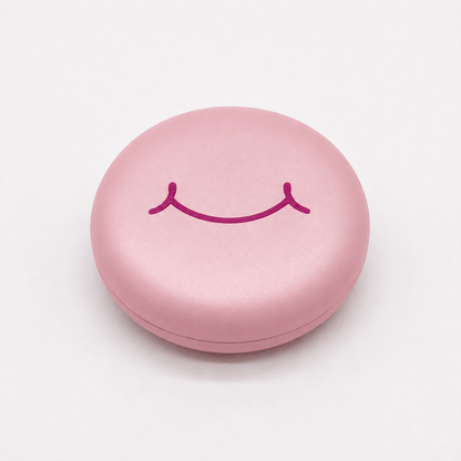 A round pink hard retainer case with a simple embossed smiley face on top, photographed on a clean white background.  Also good for clear aligner case.