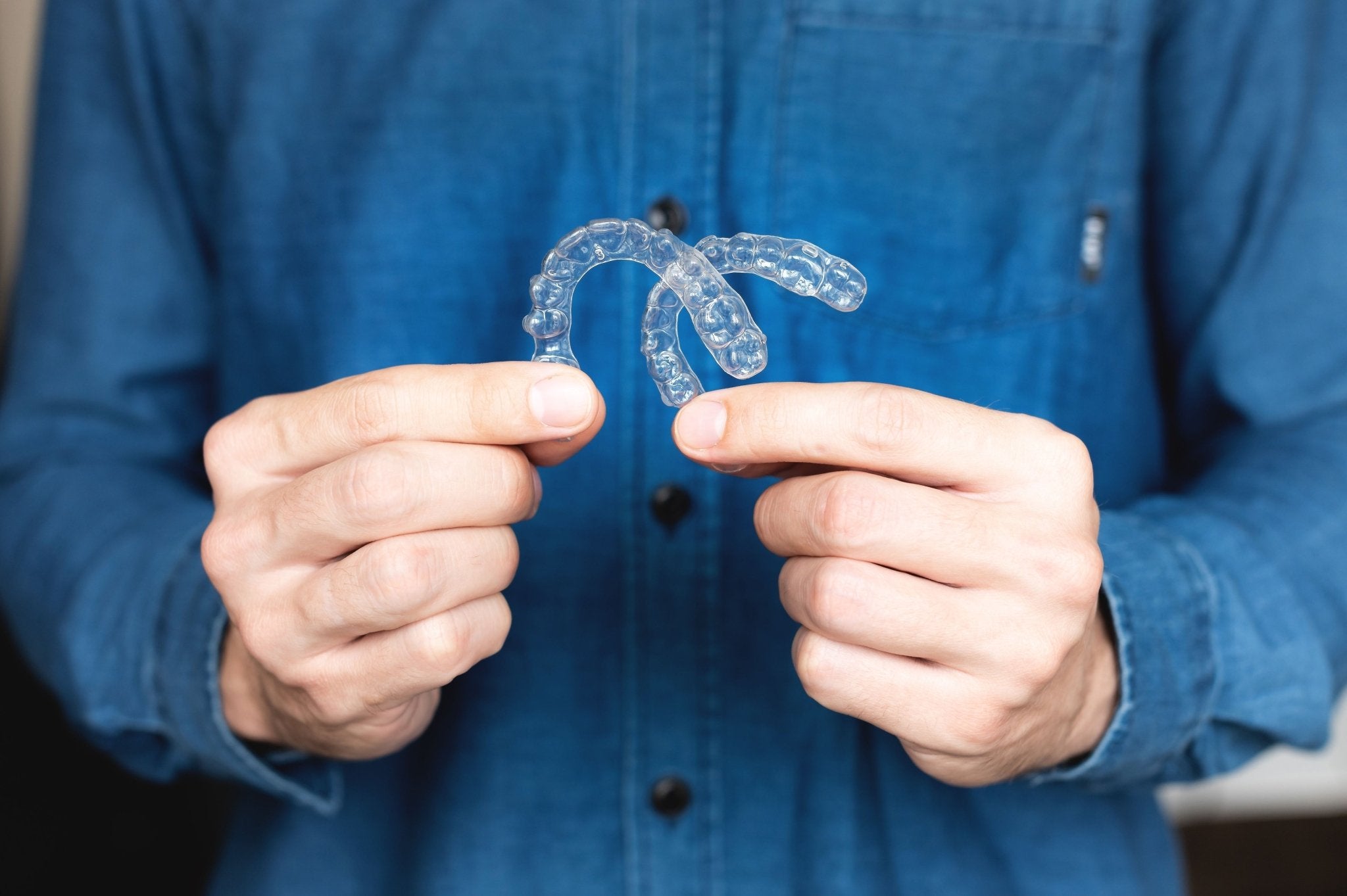 Man holding a set of clear dental retainers, showcasing their use for keeping teeth aligned after orthodontic treatment.