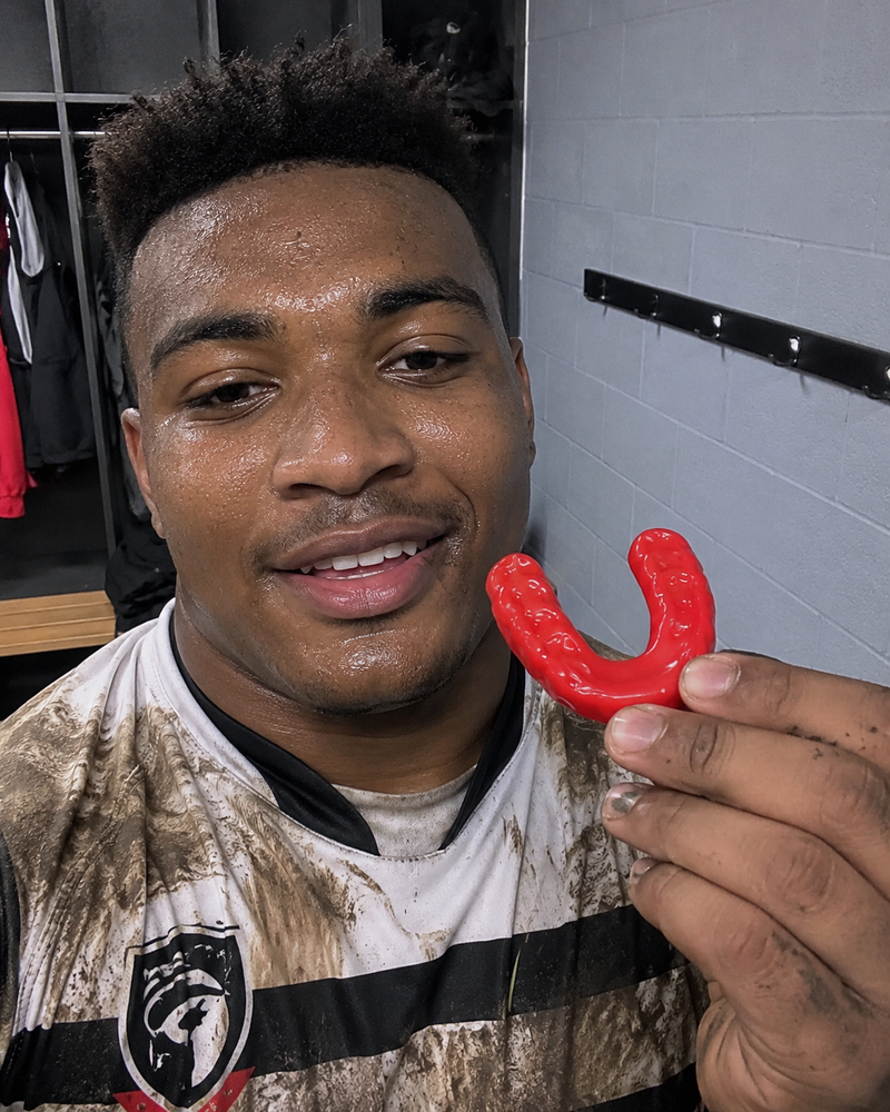 Rugby player holding a red mouthguard beside his face